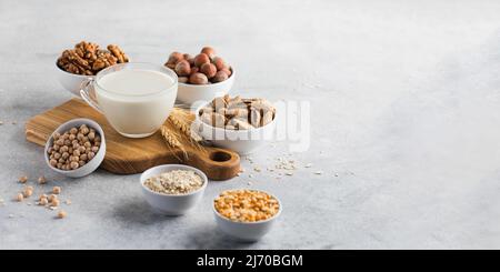 Gemüsemilch in einem Becher auf dem Hintergrund von Schüsseln mit Nüssen, Haferflocken und Hülsenfrüchten. Speicherplatz kopieren. Stockfoto