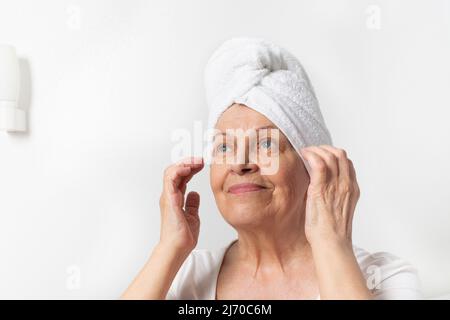 Kaukasische ältere Frau mit Falten mit weißem Handtuch kümmert sich um ihr Gesicht Stockfoto