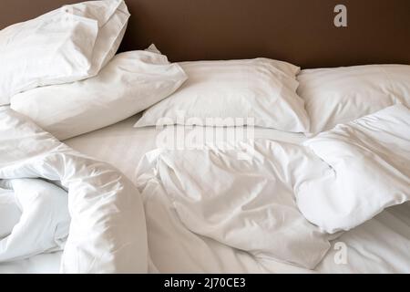 Die Inneneinrichtung des Hotelzimmers am Morgen mit einem unordentlichen Bett. Zerknitterte weiße Bettwäsche, Kissen und Decke auf dem Bett Stockfoto
