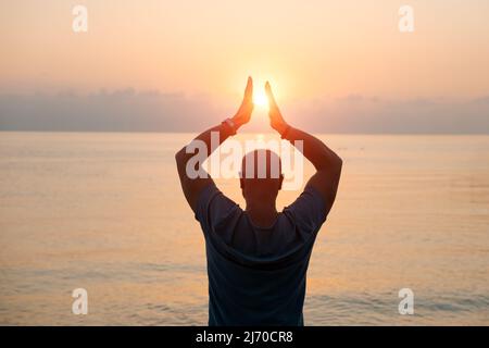 Silhouette Mann mit seinen Händen angehoben bei Sonnenuntergang am Strand Arme nach Seiten in Richtung der Sonne, Konzept für Religion, Anbetung, Gebet und Lob und Erfolg im Leben, Frieden und Ruhe in der Natur Stockfoto