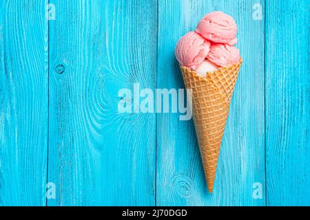 Erdbeereis in einem Waffelkegel auf blauem Hintergrund. Stockfoto