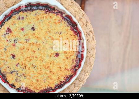 Runde Beerenkuchen in Backform auf Tischset. Bröseln Heidelbeer Schuster. Hausbacken, gesunde Mahlzeit, zuckerfreies Essen Stockfoto