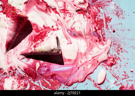 Himbeer-Eis schmelzen. Draufsicht auf leere Waffelkegel und geschmolzenes Eis mit rosa Puder, die wunderschöne Muster schaffen Stockfoto