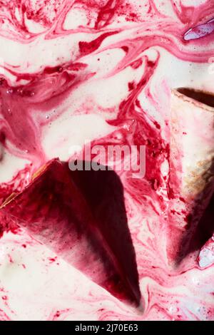 Nahaufnahme der Waffelkegel, die in geschmolzenem Himbeer-Eis mit rosa Mustern liegen Stockfoto