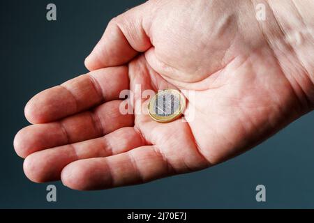 Eine Euro-Münze in männlicher Handfläche, grauer Hintergrund aus der Nähe. Stockfoto