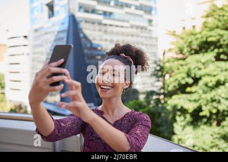 Eine junge Frau macht ein Selfie auf dem Balkon eines Stadtgebäudes Stockfoto