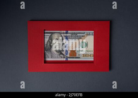 Eine 100-Dollar-Banknote in einem roten Papprahmen auf grauem Hintergrund. Stockfoto