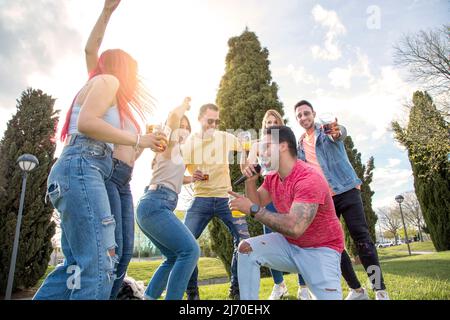 Junger Mann, der mit einem Mikrofon singt, mit einer Gruppe von Freunden, die auf einer Party im Freien tanzen Stockfoto