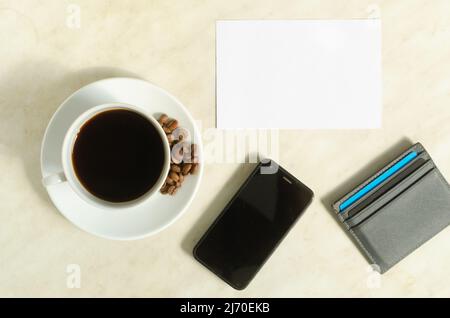 Eine Tasse Kaffee mit Kaffeebohnen, Handy, Bankkarten und leerem Rohling auf dem Tisch. Stockfoto