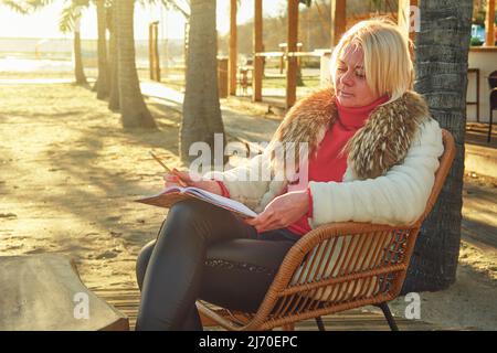 Eine Frau mittleren Alters mit blonden Haaren sitzt in einem Straßencafé. Stockfoto