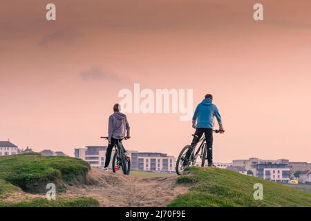 Zwei kleine Jungen auf ihren Fahrrädern auf einer rauen Sandspur bei Fistral in Newquay in Cornwall. Stockfoto