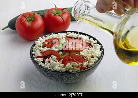 Gießen von Olivenöl Salat mit frischen Tomaten, Gurken, Quark und schwarzem Kreuzkümmel Stockfoto