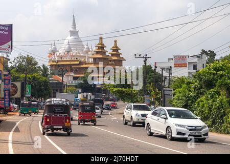 Malabe, Sri Lanka - 4. Dezember 2021: Straßenansicht mit Autos, Tuk Tuks und Mahamevnawa Amawatura Kloster auf einem Hintergrund Stockfoto