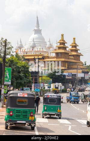 Malabe, Sri Lanka - 4. Dezember 2021: Vertikales Straßenbild mit Autos, Tuk Tuks und Mahamevnawa Amawatura Kloster auf einem Hintergrund. Gewöhnliches Peo Stockfoto