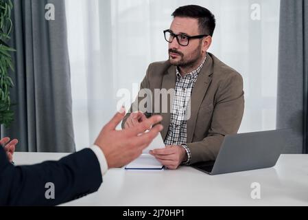 Selbstbewusster junger Manager, der sich mit einem Geschäftspartner trifft, plant die Strategie der männlichen Mitarbeiter, die im Büro am Schreibtisch sitzen. Stockfoto