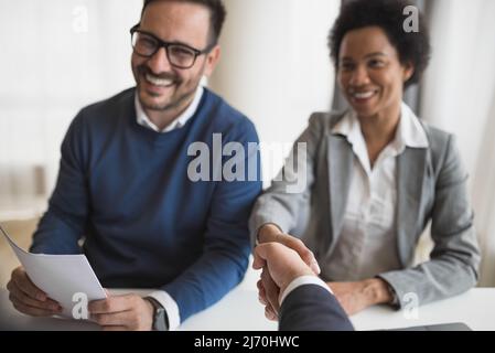 Glückliche Geschäftspartner, die in Meetings Handschlag geben, lächelnde Berufstätige, die am Schreibtisch sitzen, feiern einen erfolgreichen Abschluss bei cor Stockfoto