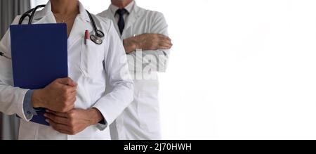 Mittelteil der Gesundheitsfachkräfte mit Berichten, männliche und weibliche Ärzte stehen vor weißem Hintergrund, sie tragen Laborkittel. Stockfoto