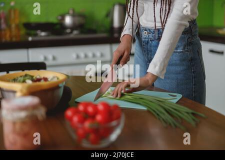 Weibliche Hände halten Messer schneiden frische Frühlingszwiebeln auf Silikonbrett innen in der Küche Stockfoto