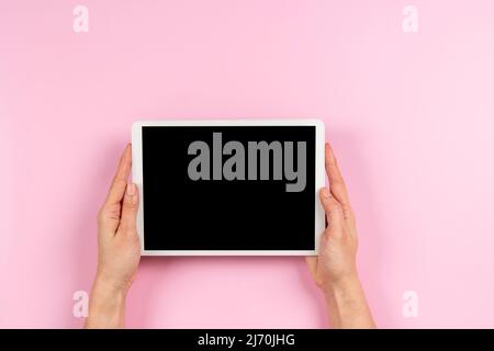 Frau Hand hält digitalen Tablet-Computer mit leerem Bildschirm Modell auf pastellrosa Hintergrund. Draufsicht, Kopierbereich Stockfoto