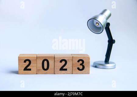 Jahr 2023 auf Holzblöcken mit silbernem Lampenhintergrund. Konzept für das neue Jahr 2023. Stockfoto