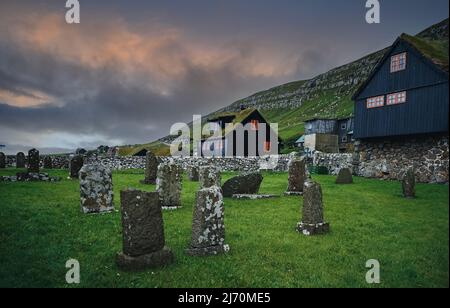 Schöner wolkig Sonnenuntergang auf traditionellen Rasenhäusern im Dorf Kirkjubour. Typische schwarze Häuser auf den Färöern, Dänemark, Nordeuropa. Stockfoto