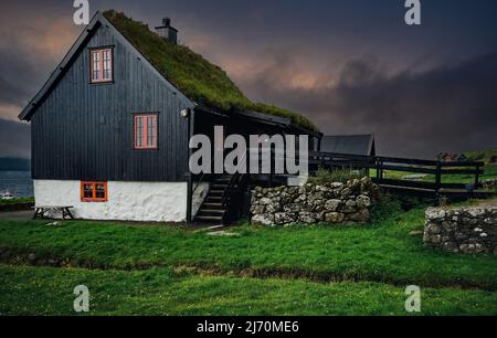 Schöner wolkig Sonnenuntergang auf traditionellen Rasen Haus in Dorf Kirkjubour. Typisches Schwarzes Haus auf den Färöern, Dänemark, Nordeuropa. Stockfoto