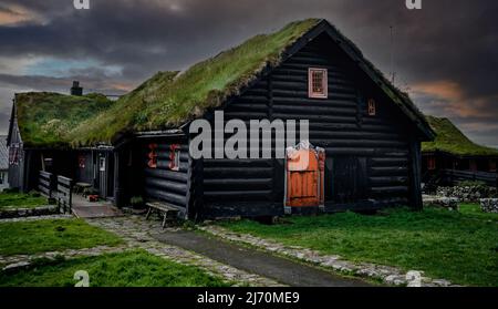 Schöner wolkig Sonnenuntergang auf traditionellen Rasen Haus in Dorf Kirkjubour. Typisches Schwarzes Haus auf den Färöern, Dänemark, Nordeuropa. Stockfoto