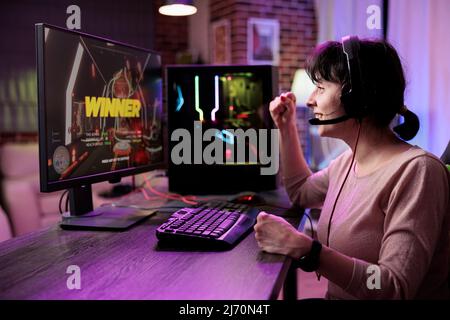 Glückliche Frau gewinnt Video-Spiele-Turnier im Live-Stream, mit Computer, um Spaß in rpg-Meisterschaft mit mehreren Spielern zu haben. Weibliche Gamer feiert Action gameplay Herausforderung gewinnen. Stockfoto
