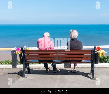 Rückansicht eines älteren Paares, das auf dem Sitz, der Bank, mit Blick auf das Meer von der oberen Promenade in Saltburn am Meer sitzt. VEREINIGTES KÖNIGREICH Stockfoto