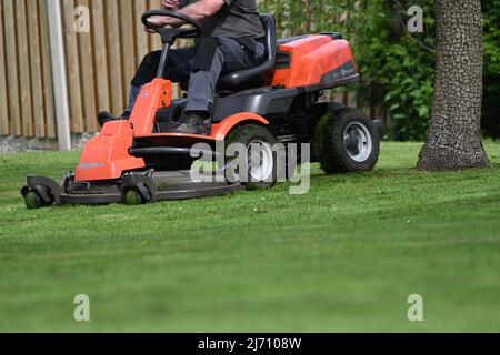 Ein Mann mäht einen Rasen auf einer Fahrt auf dem Mäher an einem Frühlingstag Stockfoto