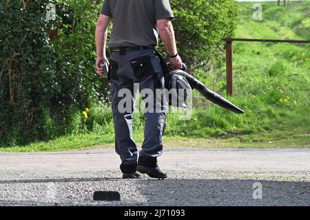 Ein Mann, der ein Laubgebläse auf einem Zufahrtsgebläse auf eine ländliche Straße ausnutzt Stockfoto