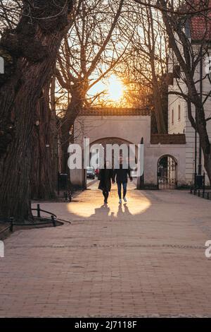 Danzig,PL-15 Mar 22: Im Olivenpark in goldener Stundensonne hinter ihnen, männliche und weibliche Paraden auf einem Gehweg in Sonnenuntergang goldene Stunde Zeit im Frühjahr mit Stockfoto