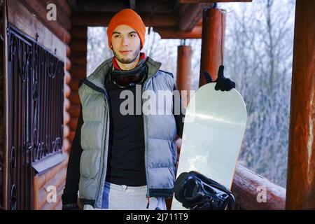 Ein Mann in einem orangenen Hut hält im Winter während eines Winterurlaubs in den Bergen eine Tasse Tee in den Händen Stockfoto