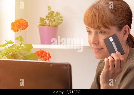 Kaukasische Frau mittleren Alters, die online mit Kreditkarte zu Hause mit einem Laptop über das Internet einkauft Stockfoto