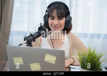 Frau, die am Schreibtisch mit Handgesten ausdrucksstark in ein Mikrofon spricht. Stockfoto