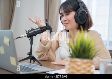 Frau, die am Schreibtisch mit Handgesten ausdrucksstark in ein Mikrofon spricht. Stockfoto