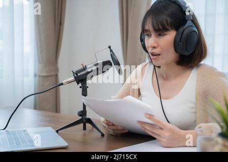 Frau, die am Schreibtisch mit Handgesten ausdrucksstark in ein Mikrofon spricht. Stockfoto