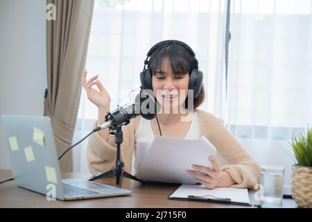 Frau, die am Schreibtisch mit Handgesten ausdrucksstark in ein Mikrofon spricht. Stockfoto