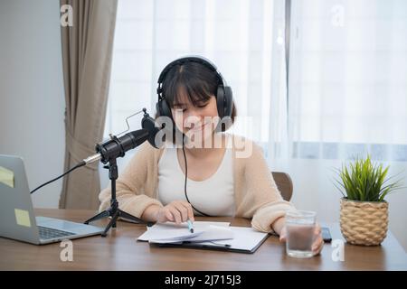 Frau, die am Schreibtisch mit Handgesten ausdrucksstark in ein Mikrofon spricht. Stockfoto