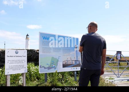 Mann liest die Informationstafel des Mull of Galloway Lighthouse, der am südlichsten Punkt Schottlands steht. Stockfoto