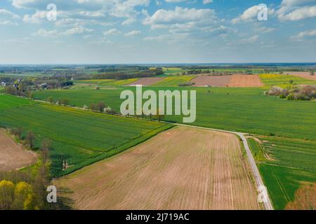 Eine weite Ebene, die mit Ackerfeldern und Wiesen bedeckt ist. An einigen Stellen kann man Baumklumpen sehen. Der Himmel ist leicht bewölkt. Foto von der Drohne. Stockfoto