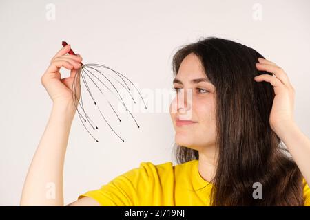 Eine Frau mit einem flexiblen Massagegerät aus Metall zur Selbstmassage des Kopfes auf weißem Hintergrund, kopieren Sie den Ort für den Text Stockfoto