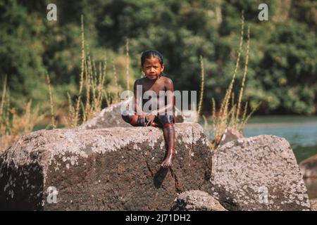 Indischer Junge aus dem Stamm des Amazonas, der auf einem Felsen am Xingu-Fluss in Brasilien sitiing, 2010. Stockfoto