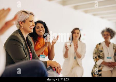 Lächelnde Geschäftsfrauen applaudieren ihren Kollegen während einer Konferenz an einem modernen Arbeitsplatz. Gruppe erfolgreicher Geschäftsfrauen, die zusammenarbeiten Stockfoto