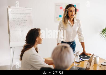 Junge Geschäftsfrau, die eine Sitzung in einem Sitzungssaal leitet. Glückliche junge Geschäftsfrau, die ihre Ideen mit ihrem Team teilt. Gruppe von multikulturellen Geschäftsfrauen Stockfoto
