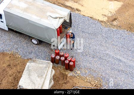 Lieferung von Propan in roten Gasflaschen auf eine Baustelle, zum Schneiden von Metall und Erhitzen von Metallrohlingen, um diese nach p zu biegen Stockfoto