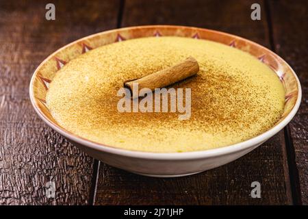 Schale mit Maismarmelade namens Curau, jimbelê oder Hominy, verziert mit Zimt in Rinde und Zimtpulver. Typisches Dessert der ländlichen Feste im Juni und Stockfoto