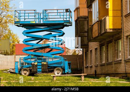 Scherenhubbühne für die Renovierung der Hausfassade. Reparatur der Fassade eines alten Gebäudes mit einem hohen Scherenlift mit einer Plattform. Stockfoto