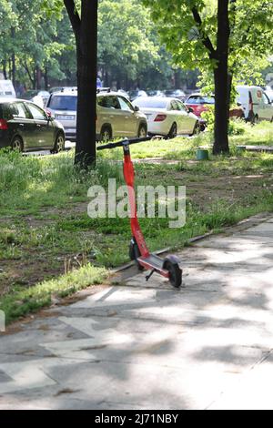 Orange elektrische Stufe, verlassen im Park entlang der Straße mit geparkten Autos in Bukarest, Rumänien Stockfoto