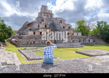 Eine junge Touristenfrau, die sitzt und die maya-Ruinen des Tempels der fünf Stockwerke betrachtet, Edzna, archäologische Stätte in Yucatan, in der Nähe von Campeche, Mexiko Stockfoto